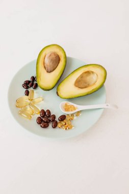 Sağlık ve diyet konsepti. Avokado ve kapsüllerdeki balık yağı D vitamini ve beyaz arka plandaki bir tabakta omega-3 yağ asitleri için.