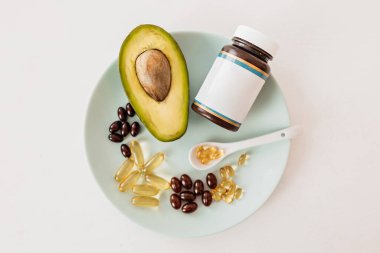 Sağlık ve diyet konsepti. Avokado ve kapsüllerdeki balık yağı D vitamini ve beyaz arka plandaki bir tabakta omega-3 yağ asitleri için.