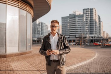 Büyük bir şehrin caddesinde gözlüklü, akıllı telefonlu yakışıklı bir adam. İş adamı şehir planıyla ilgili telefonda konuşuyor.