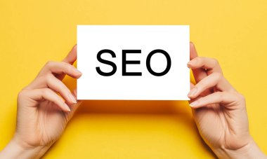 Sarı arka planda SEO yazılı kart tutan kadın elleri. İş ve finans kavramı