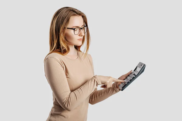 年轻漂亮的女商人戴着眼镜 手里拿着一个灰色背景的计算器 实现职业财富企业会计理念 广告的封面 — 图库照片