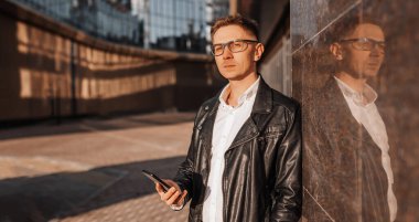 Büyük bir şehrin caddesinde gözlüklü, akıllı telefonlu yakışıklı bir adam. İş adamı şehir planıyla ilgili telefonda konuşuyor.