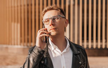 Büyük bir şehrin caddesinde gözlüklü, akıllı telefonlu yakışıklı bir adam. İş adamı şehir planıyla ilgili telefonda konuşuyor.