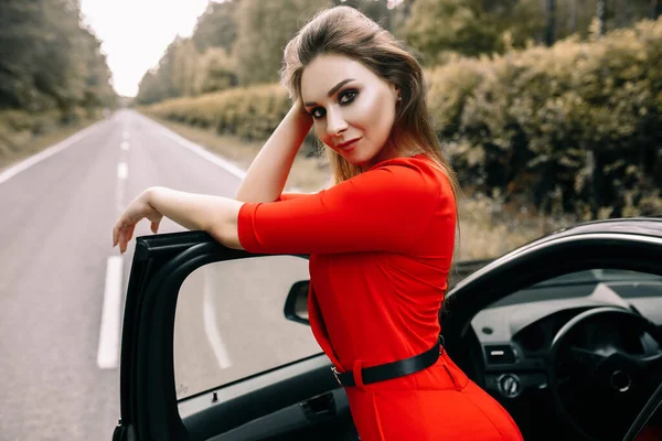 Красива Молода Дівчина Червоному Комбінезоні Стоїть Чорному Автомобілі Порожній Дорозі — стокове фото