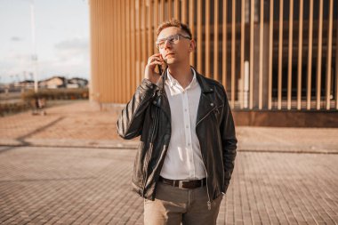 Büyük bir şehrin caddesinde gözlüklü, akıllı telefonlu yakışıklı bir adam. İş adamı şehir planıyla ilgili telefonda konuşuyor.