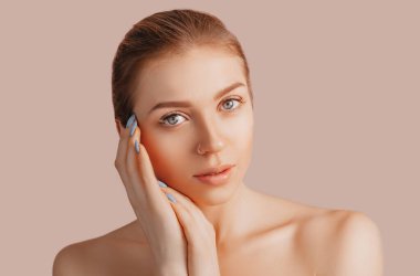 Bej bir arka planda, temiz tenli, güzel, şehvetli bir genç kız. Havlu giymiş üstsüz bir kadın. Spa tedavileri, doğal güzellik ve bakım, gençlik, krem ve maske, tazelik