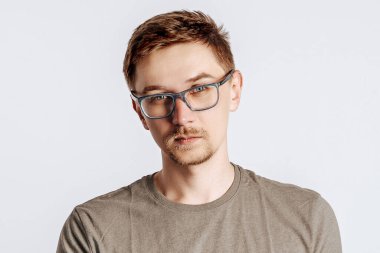 Gözlüklü, esmer sakallı genç yakışıklı adam. Öğrenci, işçi, iş adamı. Gri arka planda izole edilmiş fotoğraf için poz veriyorlar. Reklam için yer.