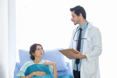 Beyaz erkek doktorlar ve kadın hastalar, hastalıktan bahsediyorlar ve hastanenin koğuşunda notlar alıyorlar.