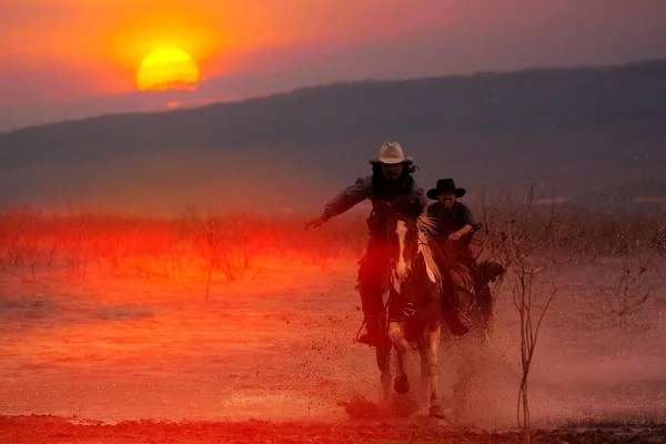 山の後ろの日没時に水の中を馬に乗ってカウボーイのシルエット — ストック写真