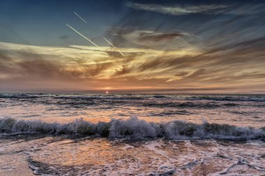 Batan güneşin ışınları deniz kıyısındaki plajları aydınlatıyor.