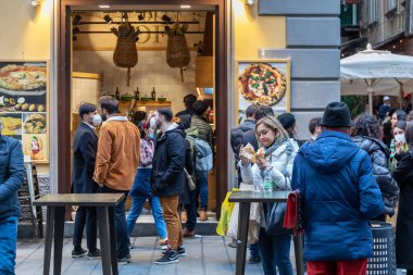 Napoli, İtalya - 24 Aralık 2021: Sokaktaki insanlar şu anda tipik bir Napoli pizzacısı önünde pişmiş yemek yiyorlar.
