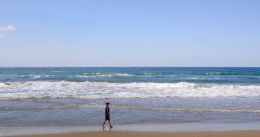 Sahilin kıyısında ayakları deniz suyuna batmış bir kadın yürüyor. Rahatlama ve özgürlük anı..