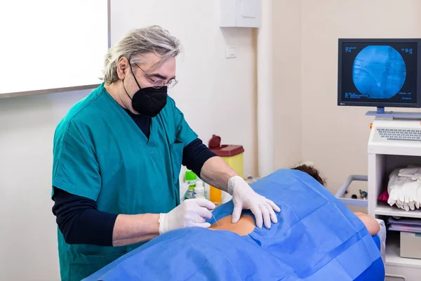 Doctor practices the infiltration of drugs to the patient in the area affected by the pain, using the ultrasound support to visualize the anatomical components of the spine.