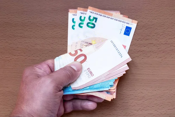 The hand holds out a bunch of 20 and 50 euro banknotes on the table