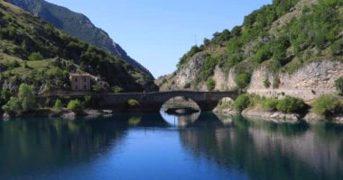 Small lake with bridge across it. Mirror of water surrounded by mountains and rocky spurs, in the green heart of an almost uncontaminated nature