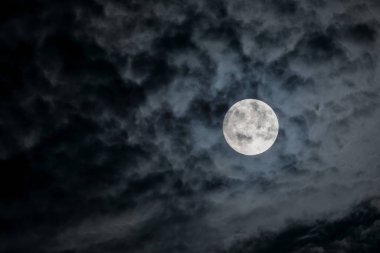 Full moon at night. The illuminated face of the moon is wrapped in a cloud cover that covers it in a veiled way.