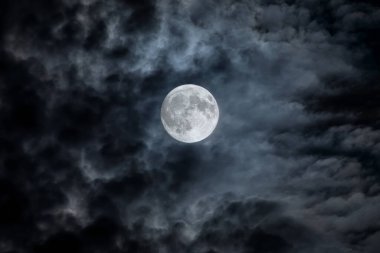 Full moon at night. The illuminated face of the moon is wrapped in a cloud cover that covers it in a veiled way.