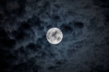Full moon at night. The illuminated face of the moon is wrapped in a cloud cover that covers it in a veiled way.