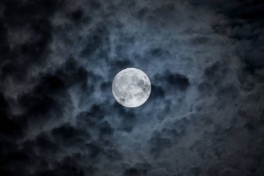 Full moon at night. The illuminated face of the moon is wrapped in a cloud cover that covers it in a veiled way.