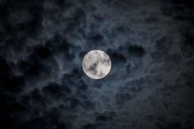 Full moon at night. The illuminated face of the moon is wrapped in a cloud cover that covers it in a veiled way.