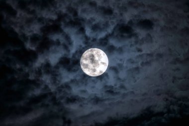 Full moon at night. The illuminated face of the moon is wrapped in a cloud cover that covers it in a veiled way.