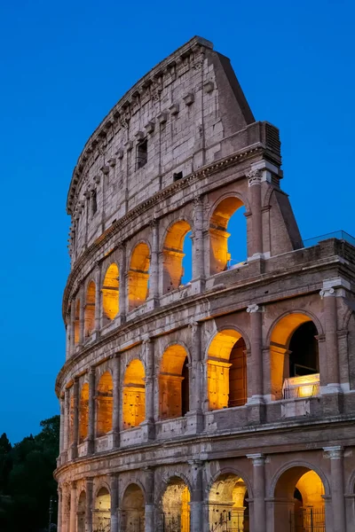 Side view of the facade of the Colosseum at dusk, with the illuminated arches.