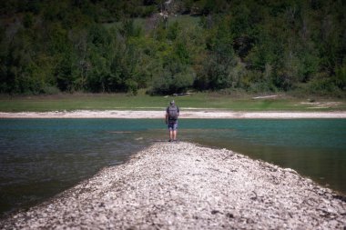 Bir yürüyüşçü göle giden bir yolda yürüyerek doğayı keşfeder. Arka planda orman var..