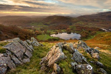 Loughrigg Tarn 'ın güzel bir sonbahar sabahında ön planda kayalarla hava manzarası. Lake District, İngiltere.