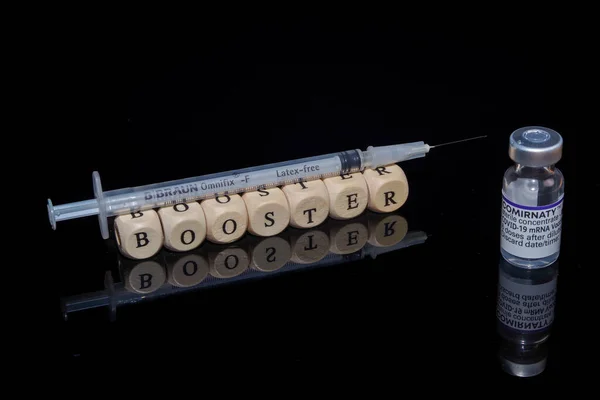 Bamberg, Alemania - 16.11.2021. Cubos de letras forman la palabra refuerzo, BioNTech-Pfizer Comirnaty vial original y jeringa — Foto de Stock