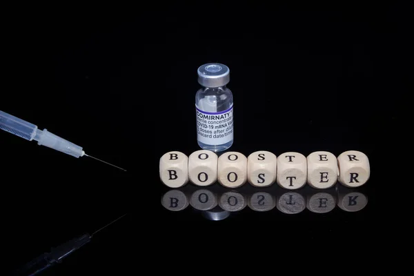 Bamberg, Alemania - 16.11.2021. Cubos de letras forman la palabra refuerzo, BioNTech-Pfizer Comirnaty vial original y jeringa — Foto de Stock