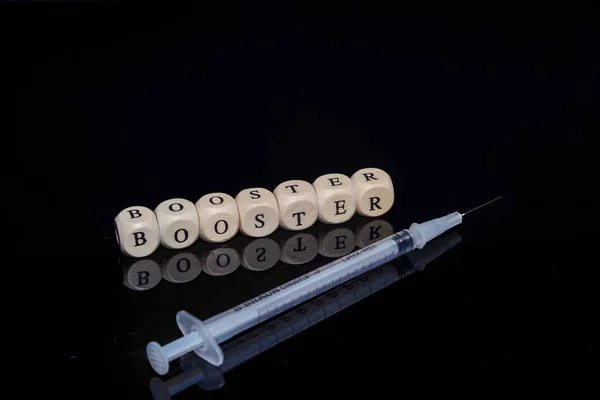 Bamberg, Niemcy - 16.11.2021. Kostki z napisem Booster i strzykawka ze szczepionką na czarnym, odblaskowym tle — Zdjęcie stockowe