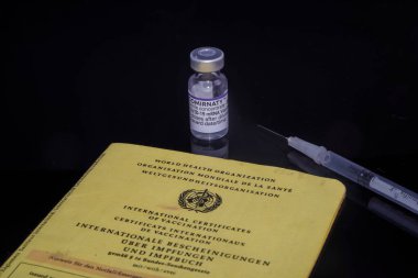 Bamberg, Almanya - 16.11.2021. Biontech-Pfizer 'dan Comirnaty şişesi ve aşı şırıngası içeren aşı sertifikası siyah, yansıtıcı arka plan
