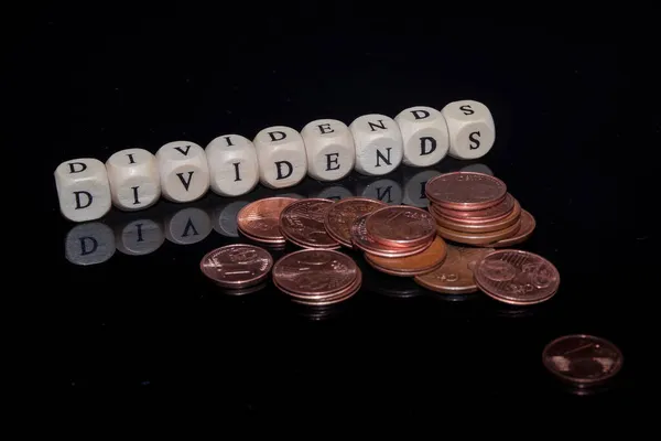 Buchstabenwürfel bilden das Wort Dividenden auf schwarzem, reflektierendem Hintergrund, Euromünzen im Vordergrund — Stockfoto