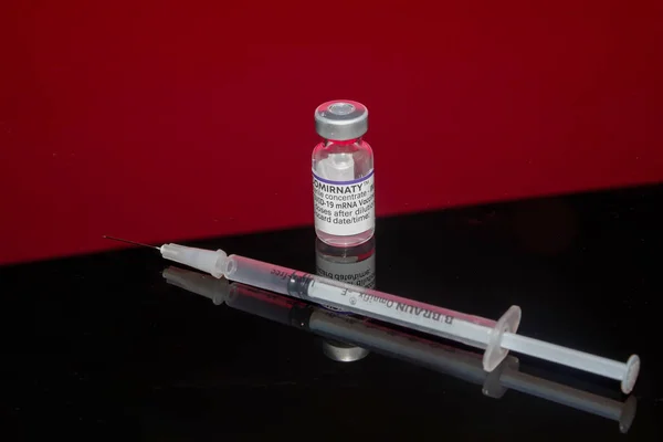 Bamberg, Almanya - 16.11.2021. Biontech-Pfizer Cormirnaty 'den bir aşı şişesi ve kırmızı ve siyah yansıtan bir arka plana karşı aşı şırıngası. — Stok fotoğraf