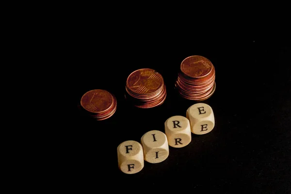 Staples of coins with wooden letters cubes forming the word FIRE in english language, concept picture with black background — Stockfoto