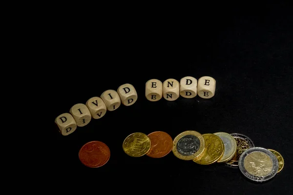 Several euro coins with wooden letters cubes forming the word "Divid Ende" in german language, concept picture for the end of dividend. — Stockfoto