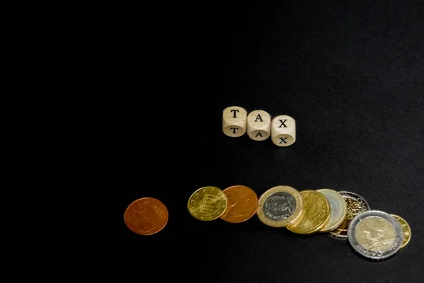 Several Euro coins with wooden letters cubes forming the word Tax in english language, concept picture with black background — Stockfoto