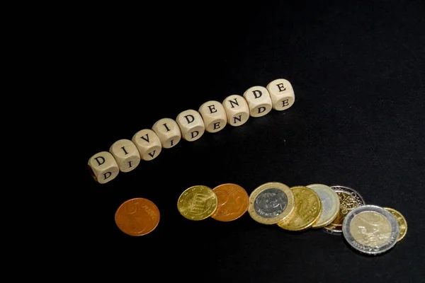 Several euro coins with wooden letters cubes forming the word Dividende in german language, concept picture with black background — Stockfoto