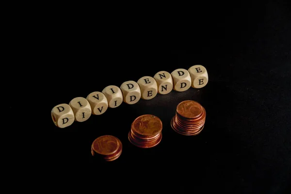 Grampos de moedas com cubos de letras de madeira formando a palavra Dividendo em língua alemã, imagem conceito com fundo preto — Fotografia de Stock