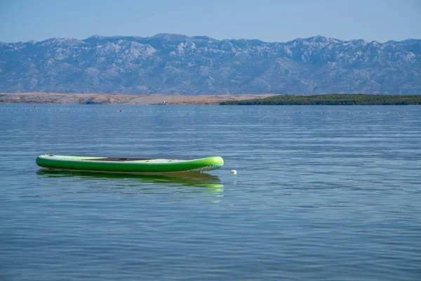 Verde e bianco Stand up Paddling Board è sdraiato sull'acqua di fronte alla costa croata — Foto Stock