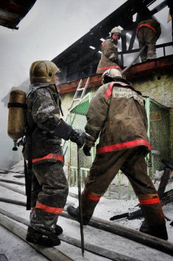 Barnaul, Rusya. 24 Aralık 2019. İtfaiyeciler soğuk bir kış gününde evin çatısındaki yangını söndürürler.