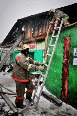 Barnaul, Rusya. 24 Aralık 2019. İtfaiyeciler soğuk bir kış gününde evin çatısındaki yangını söndürürler.