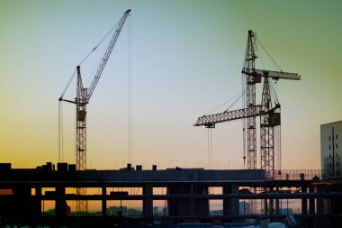 İnşaat vinçleri, günbatımı ve karanlık gökyüzünün arka planına karşı bir ev inşa ediyor.