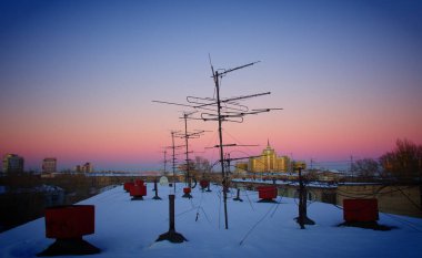 Televizyon antenleri ve elektrik kabloları akşam güneşinin arka planında.