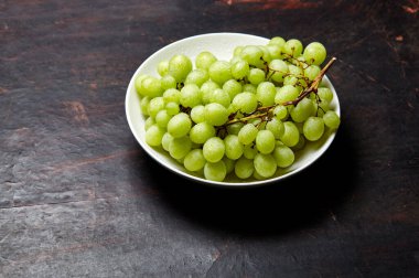 Tabakta su damlaları olan olgun yeşil üzüm dalı. Tahta arka planda sulu üzümler, yakın plan. Fotokopi alanı olan koyu mutfak masasında üzümler