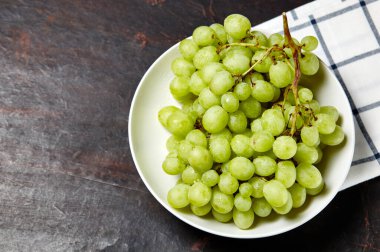 Tabakta su damlaları olan olgun yeşil üzüm dalı. Tahta arka planda sulu üzümler, yakın plan. Fotokopi alanı olan koyu mutfak masasında üzümler