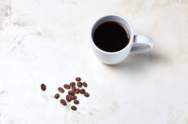 Ahşap arka planda kahve ve kahve çekirdekleri olan beyaz fincan, yakın plan. Lezzetli kahvaltı, sabah rutini konsepti