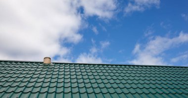 Evin çatısının inşaatı. Mavi gökyüzüne karşı metal kiremitler