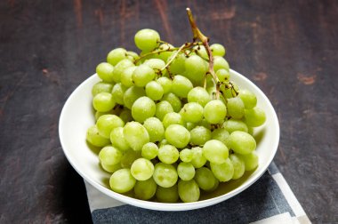 Tabakta su damlaları olan olgun yeşil üzüm dalı. Tahta arka planda sulu üzümler, yakın plan. Fotokopi alanı olan koyu mutfak masasında üzümler