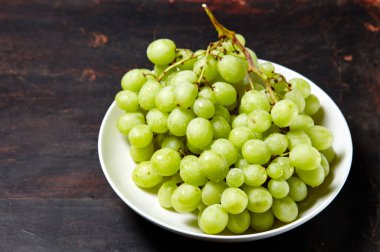 Tabakta su damlaları olan olgun yeşil üzüm dalı. Tahta arka planda sulu üzümler, yakın plan. Fotokopi alanı olan koyu mutfak masasında üzümler